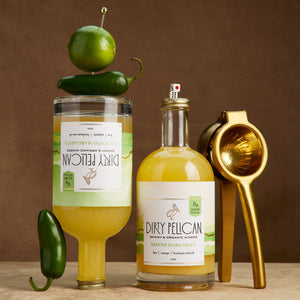 Two bottles of Dirty Pelican margarita mix with a gold juicer on a wooden surface.